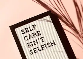 Letter board displaying 'Self Care Isn't Selfish' with artistic shadow on pink background.